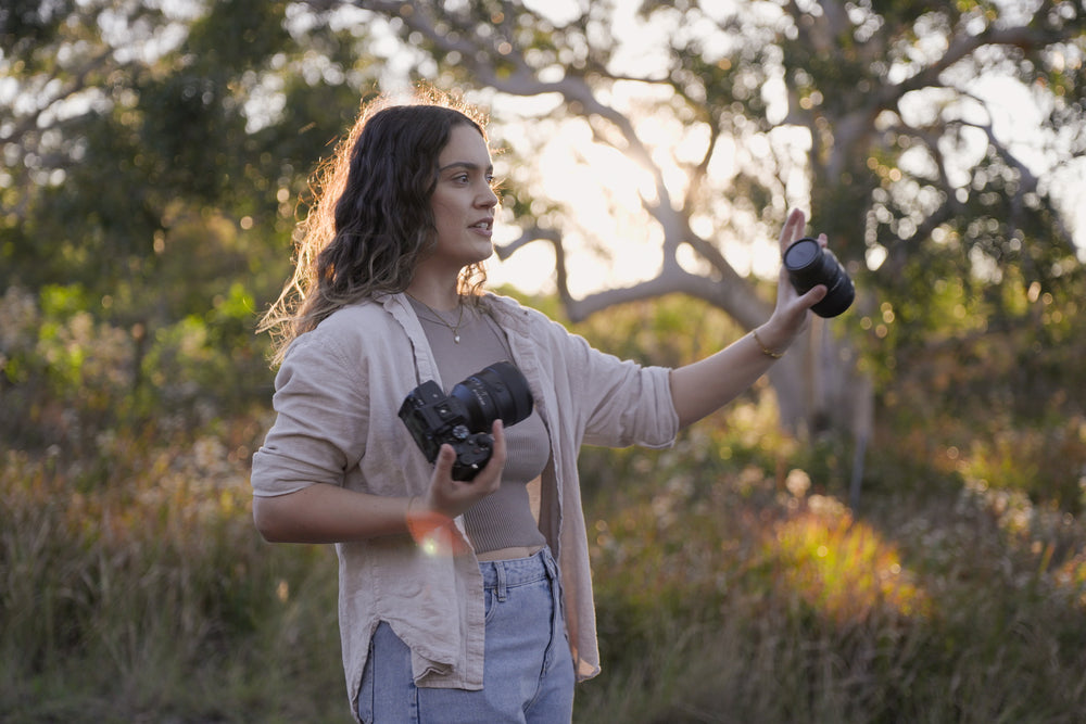 Julia Trotti explaining how to use golden hour backlight, holding her camera outdoors among trees