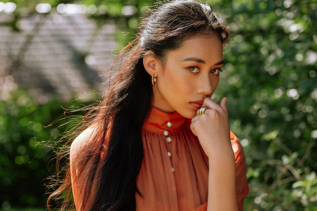 Portrait of a woman in an orange dress with her hand to her lips, shot on the LUMIX 100mm f2.8 Macro
