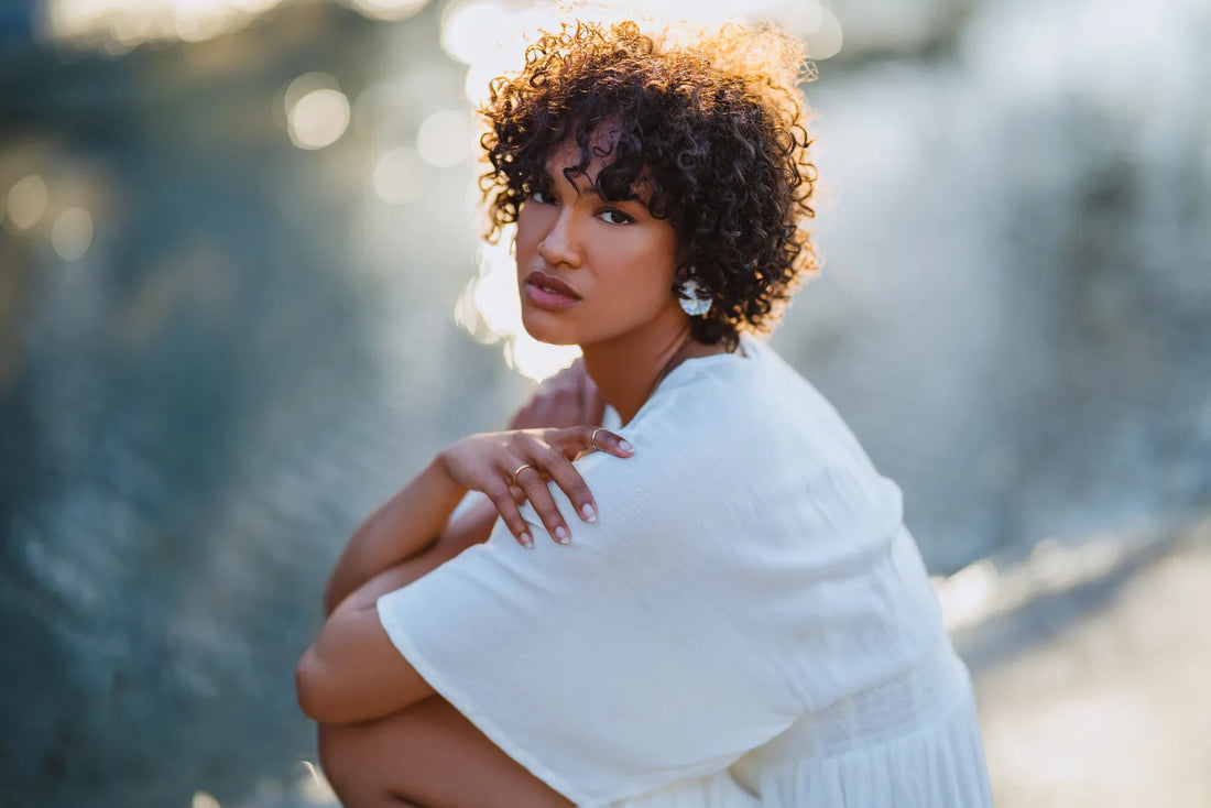 Portrait of a woman with curly hair in a white dress crouching against blue bokeh, shot on the Nikon Zf