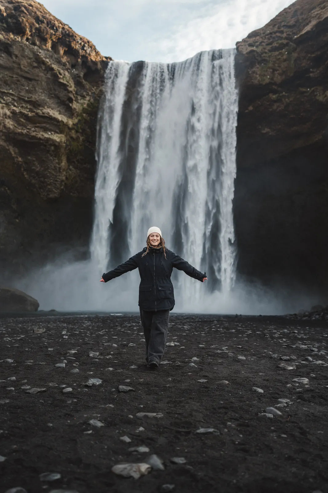 Woman with arms outstretched in front of Skógafoss waterfall